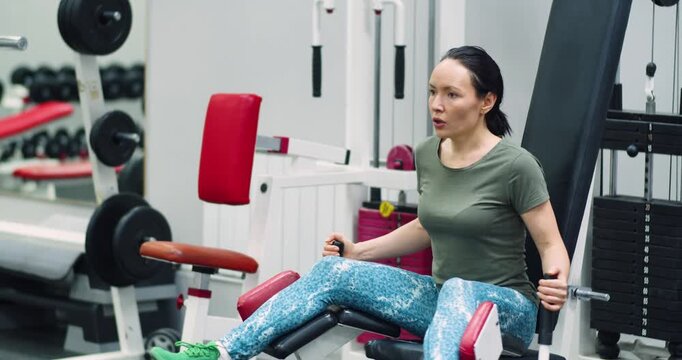 Gym workout. A middle-aged woman trains her leg muscles with the leg abduction machine, focusing on controlled, powerful movements during her gym workout. 4k footage.