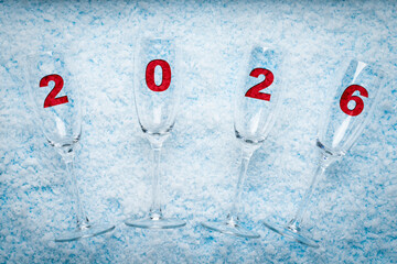 Champagne Glasses with Red 2026 Numbers on Snow Background. New Year celebrations, holiday marketing, greeting cards, event invitations