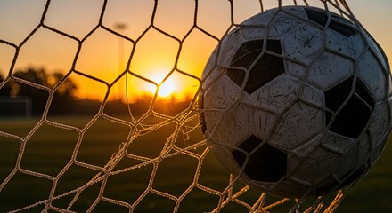 Naklejka premium Classic soccer ball nestled in the goal net with a breathtaking golden sunset illuminating the sports field during the magic hour