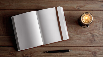 Open blank notebook with pen and candle on wooden table surface