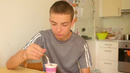 teen enjoying yogurt at kitchen table with large spoonfuls, playful mouthfuls, bright light and casual weekday