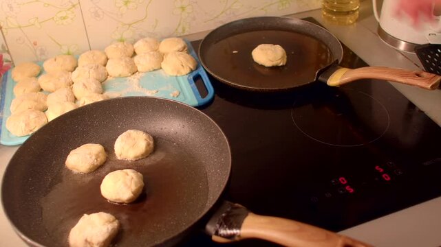 three patties landing on pan with tray of extras at side, hand places rounds with wooden spatula nearby, oil