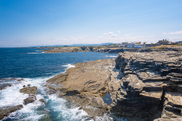 Cliffs surrounding the small fishing village of Rinlo, Lugo, Spain, with waves breaking against the rocks in the foreground