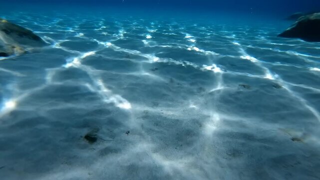 Hypnotic slow motion underwater shot of bright white sun rays creating shimmering caustic light patterns moving across a deep oceanic blue floor texture meditation, rays, zen