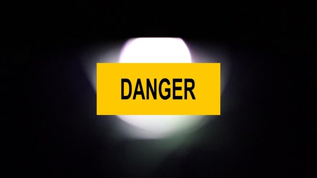 Un primer plano de un rect&aacute;ngulo de color amarillo con la palabra peligro y una luz blanca  en movimiento en un fondo negro