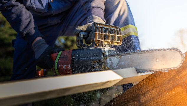 Men sawing using electrical chainsaw at roof construction