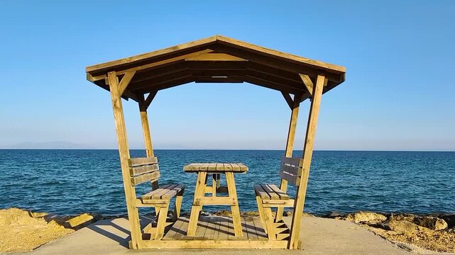 Empty wooden gazebo and picnic table overlooking the deep blue sea under a clear sky on the Aşağıkalamış beach in Şark&ouml;y.