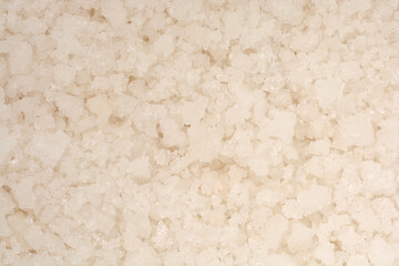 A close-up, high-angle texture shot fills the frame with coarse, irregular white and off-white granules of natural sea salt
