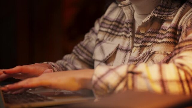 Close-up of woman with long nails typing on laptop in evening, focused on work