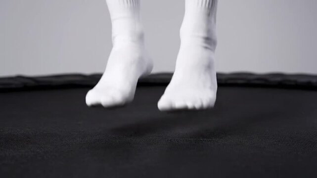 Close up of a person's bare feet wearing white athletic socks standing on a black trampoline against a light gray background with soft lighting