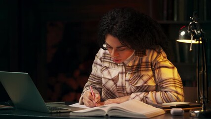 African American student taking notes during online lesson in late evening