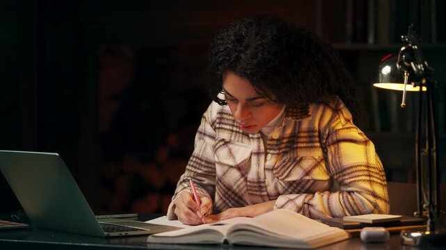 African American student taking notes during online lesson in late evening