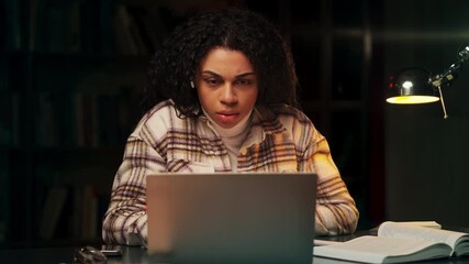 Black female student attending online video lesson and writing notes in evening