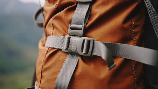 Close-up of a brown backpack strap and buckle in a natural outdoor setting with blurred greenery