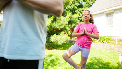 Child practicing yoga in garden with adult trainer