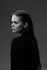 Fototapeta premium Black and white portrait of a serious woman with wet hair looking sideways with a dark background and moody lighting.
