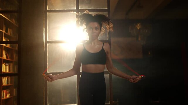 Young African American woman jumping rope in gym, cardio training hobby