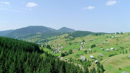 Obraz premium View above green field and village, hills and mountains