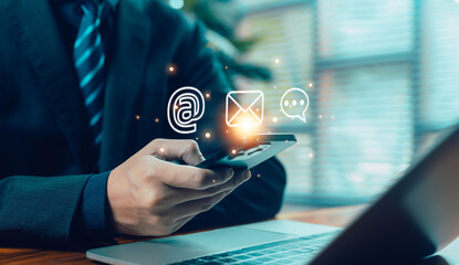 business person using a smartphone with floating digital contact icons, including email, at symbol, and chat, represents modern communication, customer support, and online connectivity in the digital