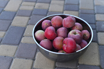 Closeup of fresh red apples in metal bowl, placed on paved surface. Vibrant apples shine in daylight highlighting healthy food concept.