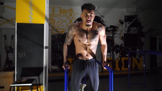 Muscular afro american sportsman doing push ups on parallel bars at modern gym. Strong african athlete with tattoos doing hard exercises at sport club. Concept of healthy and active lifestyle. Slow mo