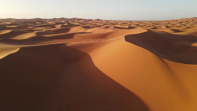 Sweeping aerial drone shot over vast sandy desert dunes changing dramatically from muted monochrome tones to rich saturated ochre colors muted, drone, earthy