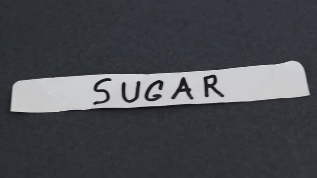 Un primer plano de un papel de color blanco con la palabra az&uacute;car en un fondo gris oscuro en movimiento
