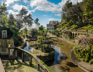 A serene garden scene in Madeira Monte Palace tropical garden in Funchal with lush greenery, a tranquil stream, and traditional architecture in the background. Ideal for nature lovers and tourists.