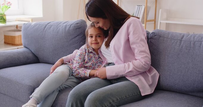 Little girl and mother hugging and talking sit on sofa and home. Loving mom embracing, stroking, kissing cute preschooler 4s daughter, enjoy time together and trustworthy conversation. Love concept