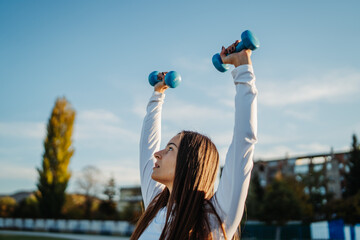 Woman exercising outdoors lifting dumbbells for strength