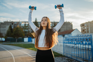 Young woman lifting dumbbells performing outdoor workout