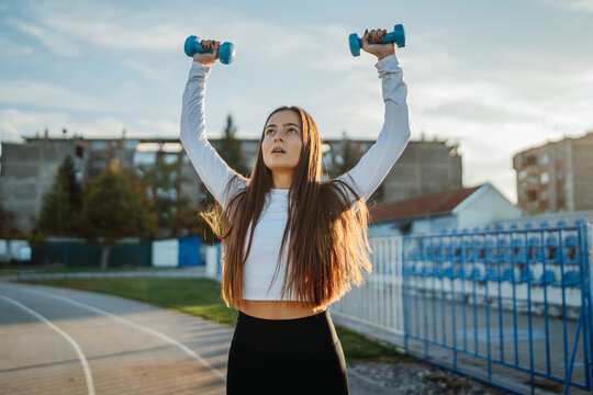 Young woman lifting dumbbells performing outdoor workout