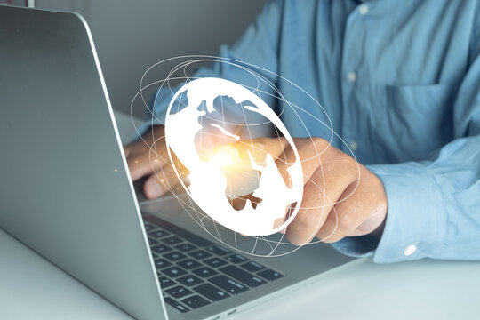 Businessman working on laptop with holographic world globe icon, representing global business connection, international network, digital internet technology, and communication concept.