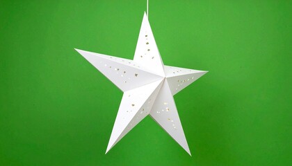 White 3D eight-point star ornament hanging on string against bright green background — festive and geometric.