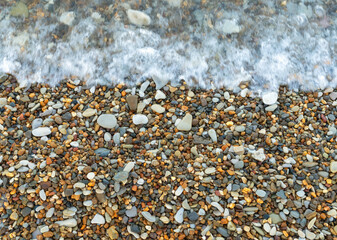 Sea wave washing over a shore covered with multicolored pebbles