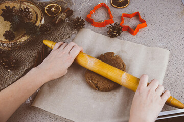 Children's hands roll out the dough on a dark old wooden background with christmas decorations and lights.