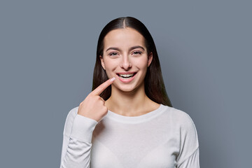 Beautiful smiling young woman showing healthy teeth on camera, on gray background
