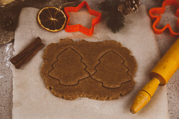 Making gingerbread cookies, Christmas holiday tradition. Raw gingerbread dough with gingerbread man shape and festive metal cutters on rustic table.