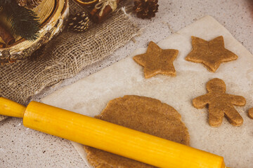Rolled ginger dough on parchment paper, On the wooden surface there are metal gingerbread molds and a rolling pin.
