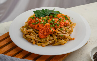 A plate of spaghetti topped with tomato sauce mixed with meat, cheese, spices, onions and lettuce leaves stands on a wooden tray.