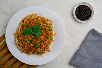 A plate of spaghetti topped with tomato sauce mixed with meat, cheese, spices, onions and lettuce leaves and black peppercorns next to it.