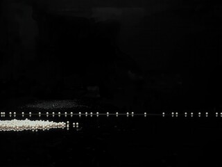 Small white pearls aligned on black surface with reflection minimal 50 characters, maximum 100