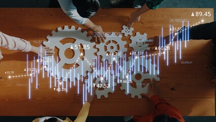 A group of diverse individuals collaborates over a table with gears and financial graphs, symbolizing innovation and strategic planning in a modern business environment. Raster