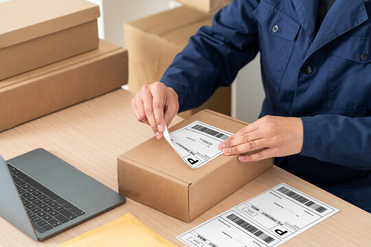 Latin man preparing a package for shipping, sticking priority mail label on a cardboard box at his startup business office