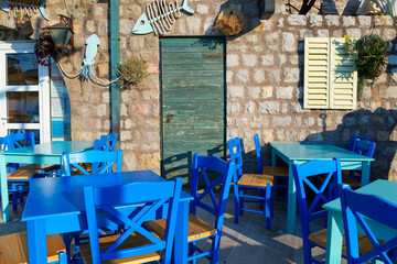 cozy outdoor cafe or restaurant with decorations, located on embankment of Petrovac city, Montenegro, tables and chairs against the background of a stone wall of an old building