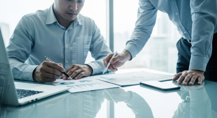 Two businessmen analyze data and reports at a bright meeting desk, reviewing documents and working together in a modern corporate office.