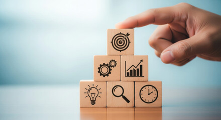 Wooden blocks stacked showing strategy symbols including target, light bulb, magnifier, gear, clock and chart over wood table and blue background. 