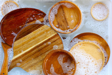 A top-down view of various wooden spoons and bowls soaking in soapy water, ready for a thorough...