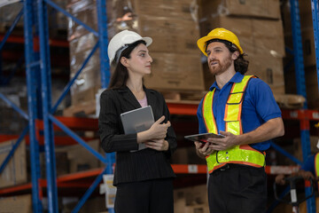 Warehouse supervisor and worker discussing logistics tasks using digital tablets in storage facility. Concept of teamwork, smart supply chain management and professional warehouse collaboration.