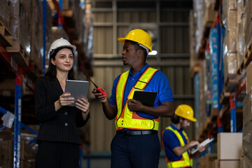 Warehouse supervisor and worker using tablet and walkie-talkie to manage inventory operations while staff inspects stock. Concept of logistics coordination, digital communication.
